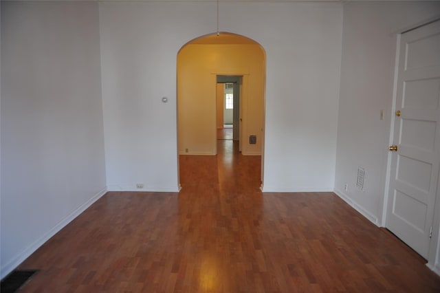 empty room featuring baseboards, arched walkways, visible vents, and wood finished floors