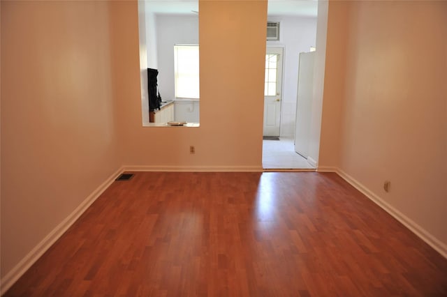 empty room with wood finished floors, visible vents, and baseboards