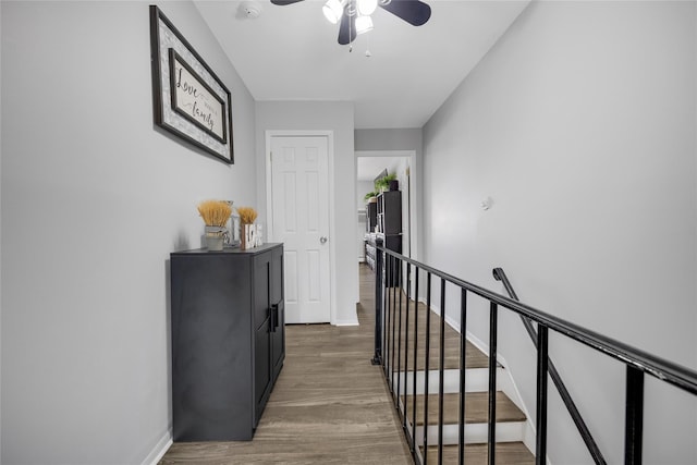 hallway with baseboards, an upstairs landing, and wood finished floors