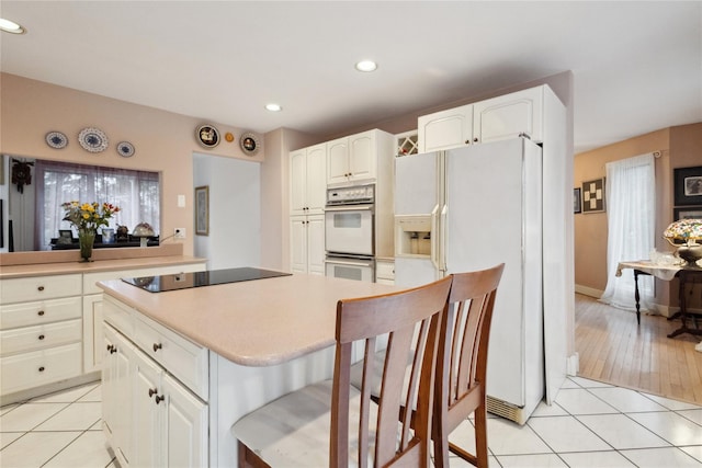 kitchen with white appliances, light tile patterned floors, a kitchen bar, white cabinetry, and recessed lighting