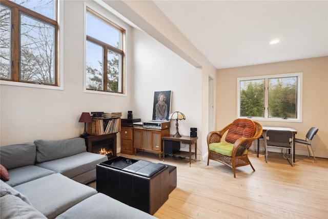 living area with recessed lighting, a warm lit fireplace, and light wood-type flooring