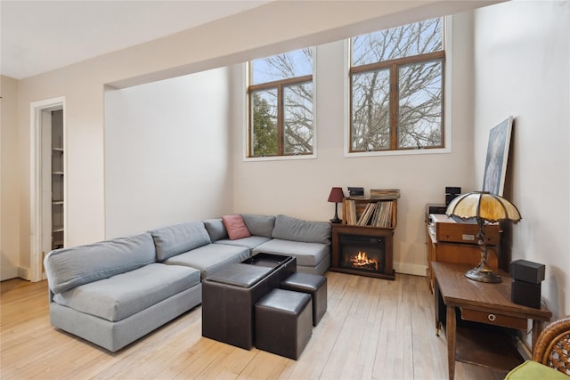 living room with baseboards, a glass covered fireplace, and light wood-style flooring