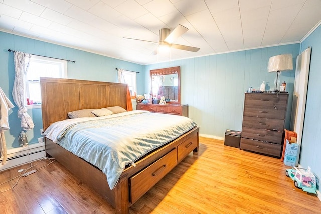 bedroom with crown molding, a baseboard heating unit, light wood-type flooring, and a ceiling fan