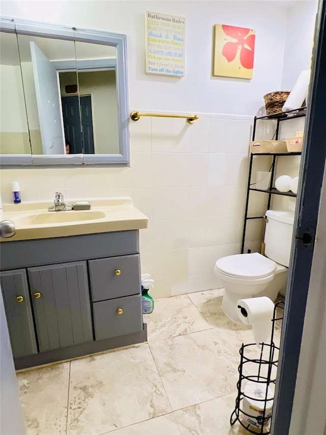 half bathroom featuring marble finish floor, tile walls, vanity, and toilet