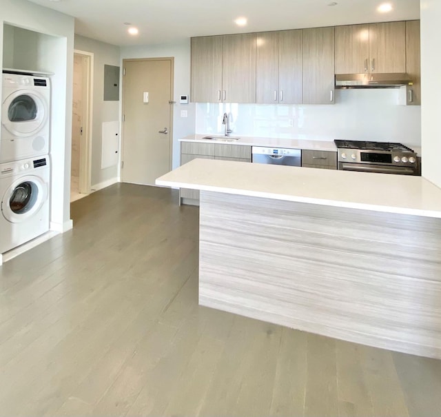 kitchen featuring extractor fan, light countertops, stacked washer and clothes dryer, stainless steel appliances, and a sink