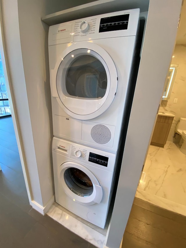 washroom featuring baseboards, stacked washer and dryer, marble finish floor, and laundry area