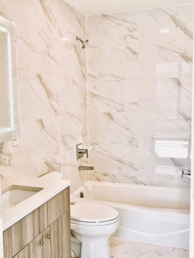 bathroom featuring toilet, vanity, shower / tub combination, marble finish floor, and tile walls