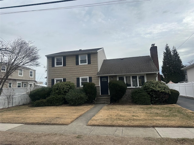 view of front of property featuring a shingled roof, a chimney, a front lawn, and fence