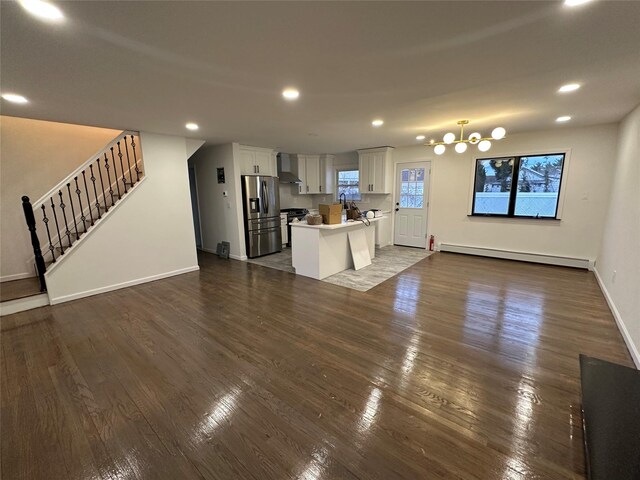 unfurnished living room with a baseboard heating unit, recessed lighting, stairway, baseboards, and dark wood-style flooring