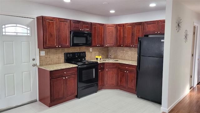 kitchen with light stone countertops, a sink, black appliances, tasteful backsplash, and reddish brown cabinets