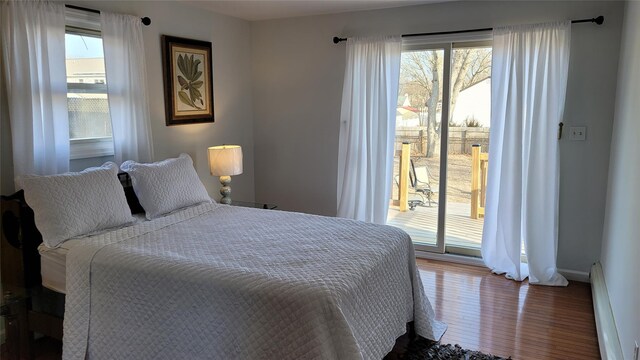 bedroom with a baseboard heating unit, access to outside, wood finished floors, and baseboards