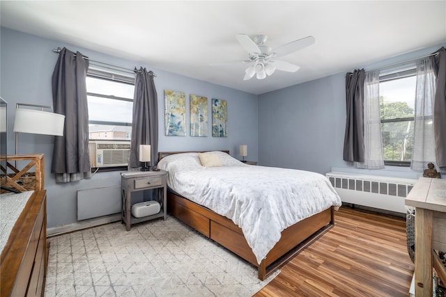 bedroom featuring a ceiling fan, radiator, cooling unit, and light wood-type flooring