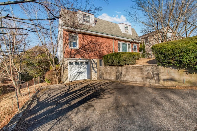 view of home's exterior featuring a garage, fence, brick siding, and driveway