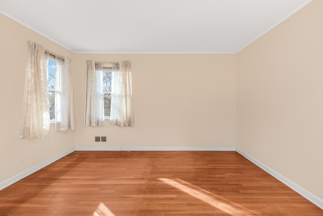 spare room with wood finished floors, visible vents, and ornamental molding