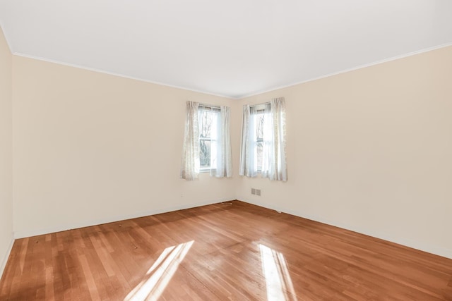 empty room featuring visible vents, crown molding, and light wood-type flooring