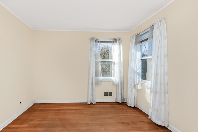 spare room featuring baseboards, wood finished floors, and crown molding