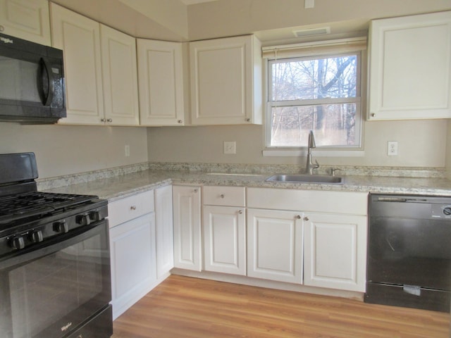 kitchen with a sink, black appliances, light wood-style flooring, and white cabinetry