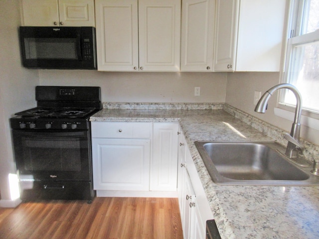 kitchen with a sink, black appliances, light countertops, light wood-style floors, and white cabinetry