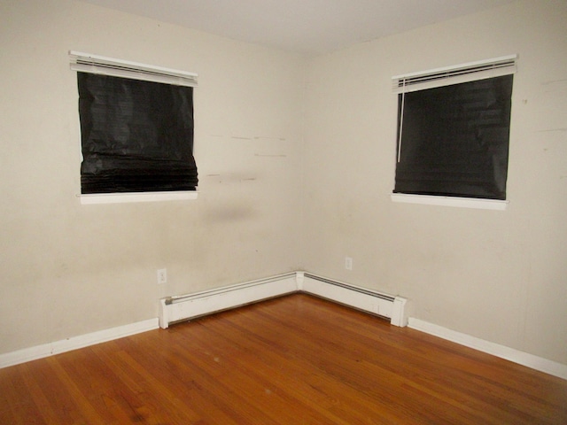 unfurnished room featuring baseboard heating, a baseboard heating unit, baseboards, and wood finished floors