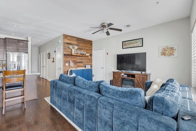 living area featuring dark wood finished floors, visible vents, wood walls, and ceiling fan