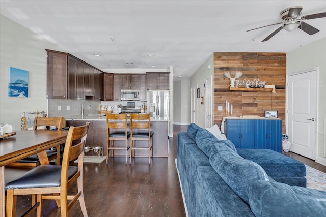 living area with a ceiling fan, wooden walls, recessed lighting, and dark wood-style floors