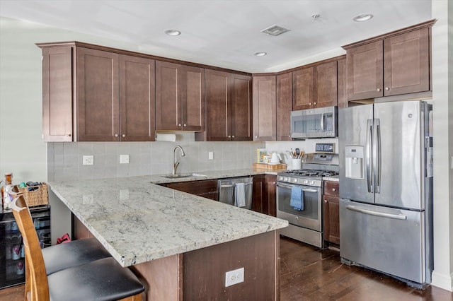 kitchen with dark wood-style floors, light stone countertops, a peninsula, a sink, and appliances with stainless steel finishes