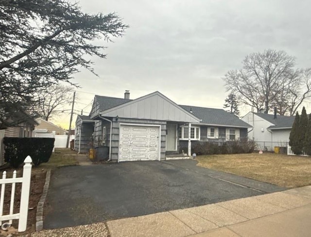 ranch-style house with a front yard, fence, a garage, aphalt driveway, and board and batten siding