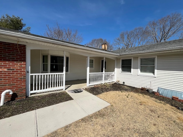 view of exterior entry featuring a porch and brick siding