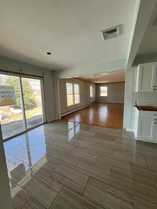 spare room featuring wood finish floors, a baseboard heating unit, and visible vents