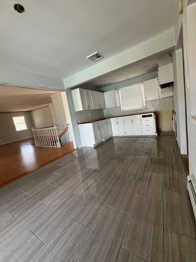 kitchen with visible vents, wood finish floors, white cabinetry, open floor plan, and backsplash