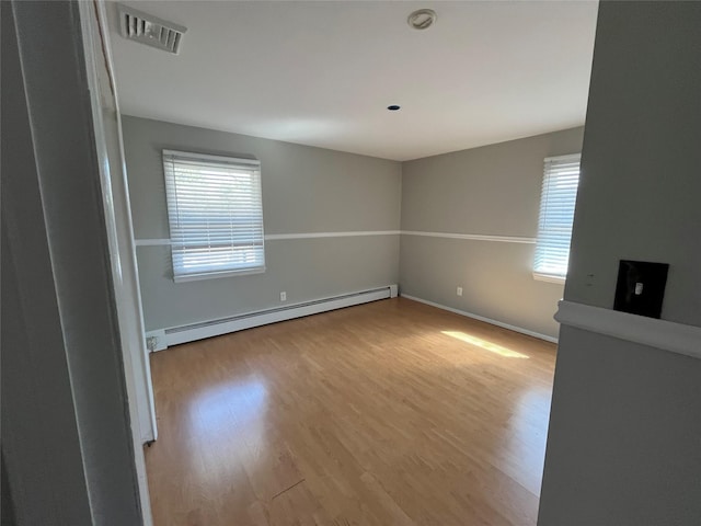 spare room with plenty of natural light, light wood-type flooring, visible vents, and a baseboard radiator