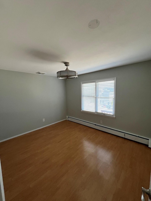 spare room with visible vents, baseboards, baseboard heating, and wood finished floors