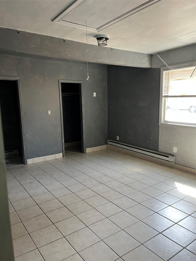 empty room featuring light tile patterned floors, baseboards, and a baseboard radiator