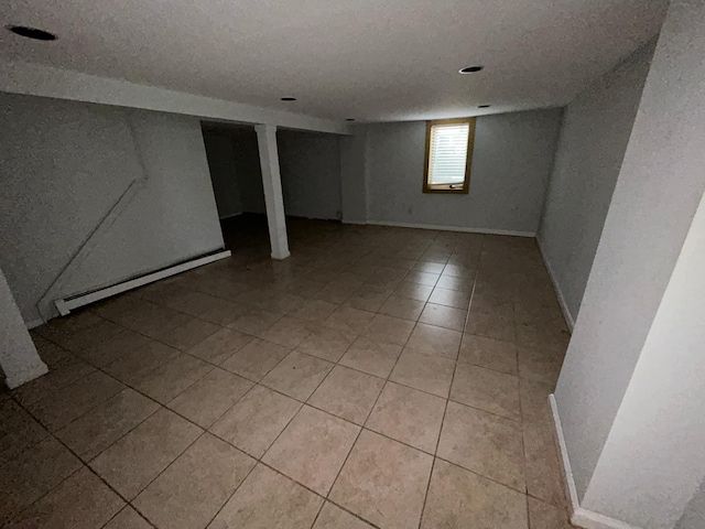 below grade area featuring light tile patterned floors, a textured ceiling, baseboards, and a baseboard radiator