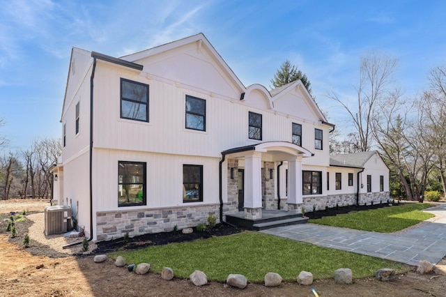 modern inspired farmhouse with stone siding, cooling unit, and a front lawn