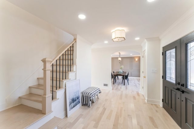 foyer featuring arched walkways, ornamental molding, stairs, french doors, and light wood-type flooring