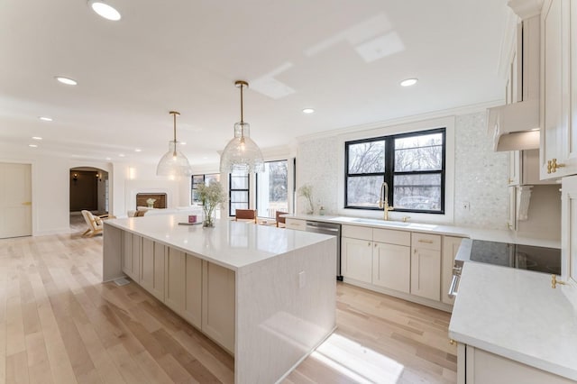 kitchen with a sink, a center island, arched walkways, light wood finished floors, and dishwasher