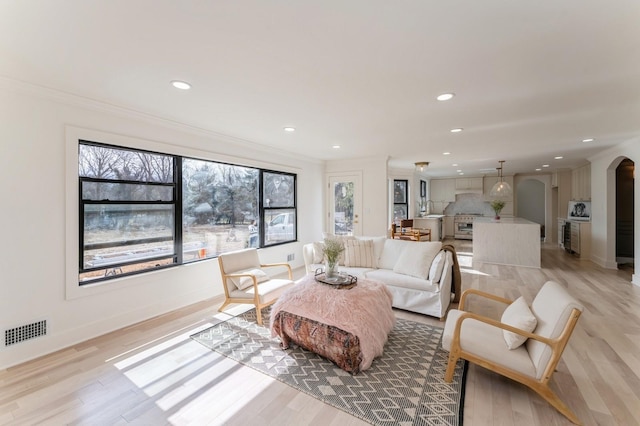 living area with light wood-style floors, crown molding, arched walkways, and visible vents