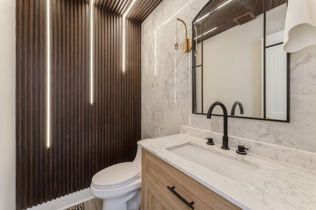 half bathroom with vanity, tile walls, and toilet