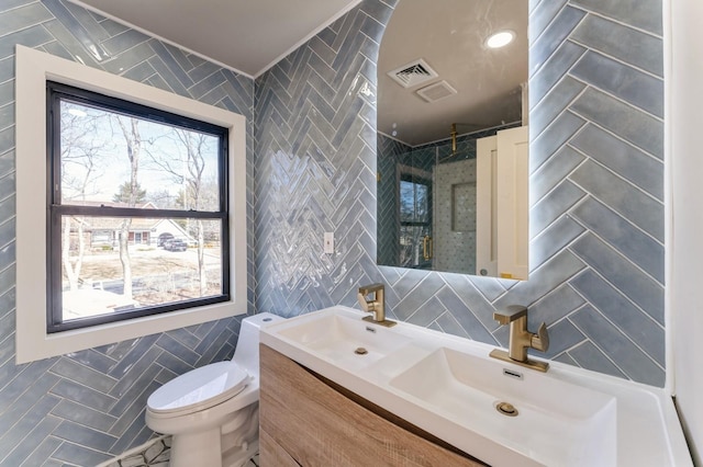 full bathroom featuring double vanity, a stall shower, a sink, tile walls, and toilet