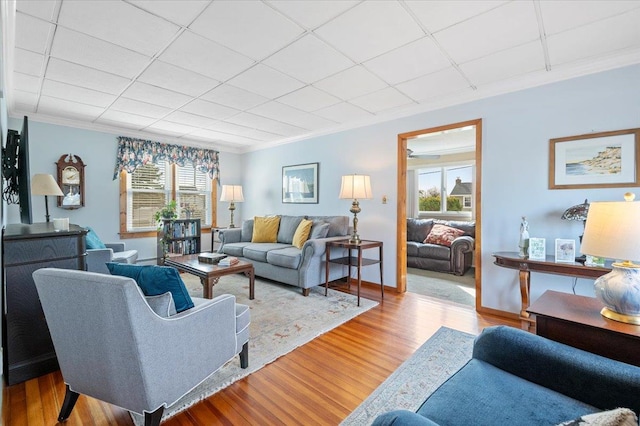 living room featuring baseboards, a paneled ceiling, wood finished floors, and ornamental molding