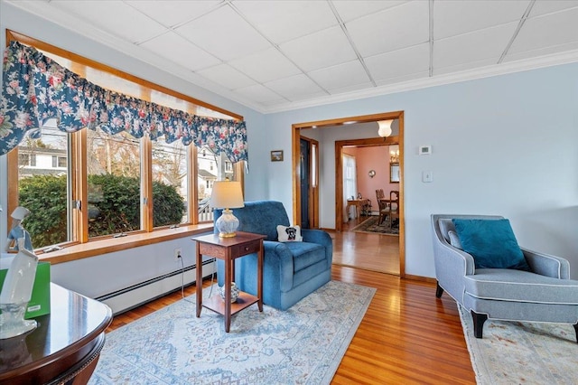 living area featuring baseboard heating, a drop ceiling, crown molding, and wood finished floors