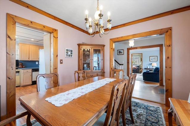 dining room with light wood-style flooring, an inviting chandelier, ornamental molding, and stairway