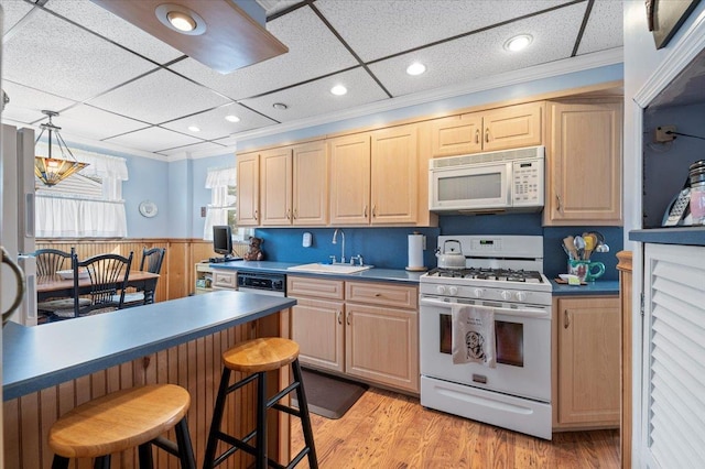 kitchen with a kitchen bar, white appliances, light brown cabinets, and a sink