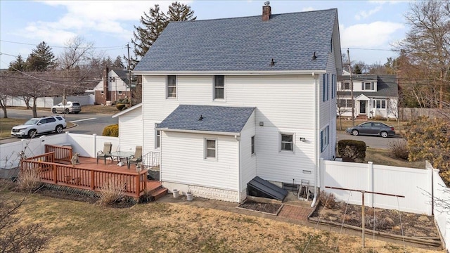 back of house featuring a lawn, a deck, fence, roof with shingles, and a chimney