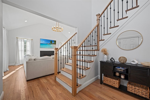 stairway featuring a fireplace, an inviting chandelier, wood finished floors, and high vaulted ceiling