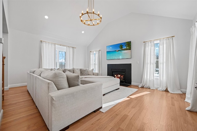 living room with baseboards, high vaulted ceiling, a fireplace with flush hearth, a notable chandelier, and light wood-type flooring