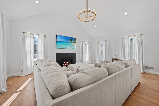 living area with visible vents, high vaulted ceiling, a glass covered fireplace, an inviting chandelier, and light wood finished floors