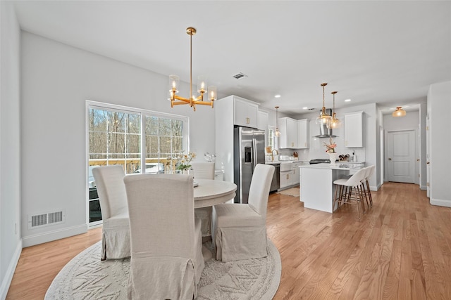 dining area featuring light wood finished floors, a notable chandelier, baseboards, and visible vents