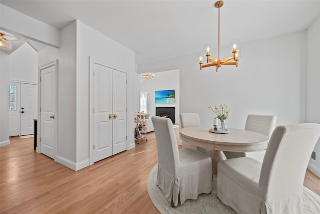 dining space featuring a chandelier, a healthy amount of sunlight, light wood finished floors, and a lit fireplace